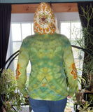 Person wearing a green tie-dye hoodie with a mandala design, standing indoors with plants in the background.
