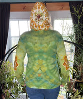 Person wearing a green tie-dye hoodie with a mandala design, standing indoors with plants in the background.