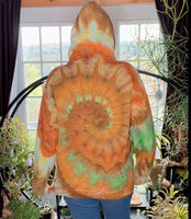 Person wearing a tie-dye hoodie with orange and green patterns in a room with plants.