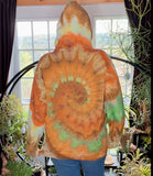 Person wearing a tie-dye hoodie with orange and green patterns in a room with plants.